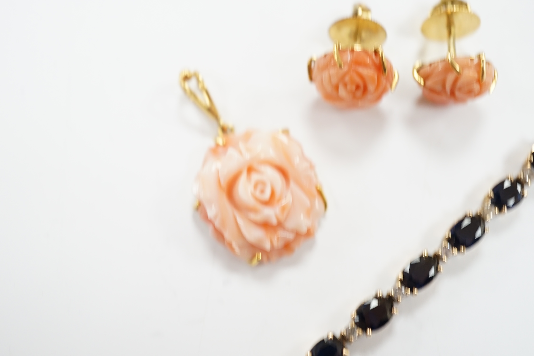 A modern 18ct and carved coral set 'rose' pendant, 16mm and a pair of matching ear studs and a yellow metal and two colour sapphire set line bracelet, 18cm.